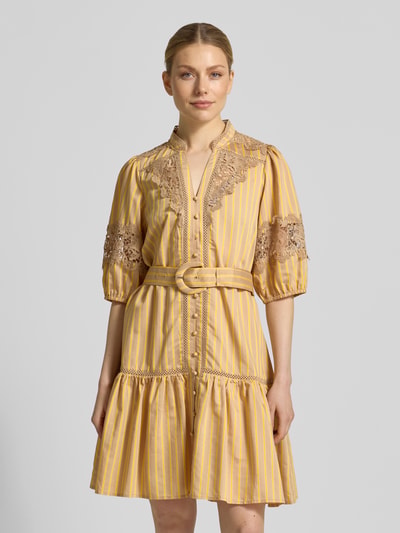 Frauenmodel trägt Knielanges Kleid mit Spitze und Gürtel Modell 'CATLEYA' von SUNCOO PARIS, gelb gestreifter Viskose-Mix, taillierter Schnitt, Spitze, Stehkragen, V-Ausschnitt, Gürtel, Vorderansicht, Nahaufnahme Oberkörper.