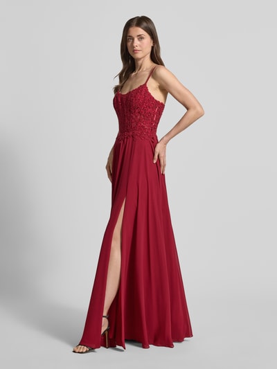 Kobiece model prezentuje wieczorową suknię z kwiatową koronką i kamieniami 'Abendkleid mit floralem Spitznbesatz' od Mascara, krój slim fit, dekolt carmen, ramiączka spaghetti, rozkloszowana spódnica z szyfonu, kryta podszewka, suwak w szwie, sznurowanie z tyłu, długość tyłu w rozmiarze 36: 152 cm, szerokość w rozmiarze 36: 40 cm, widok na całe ciało z przodu.
