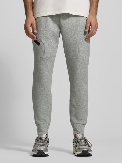 Männermodel trägt Regular Fit Sweatpants mit Logo-Print Modell 'Unstoppable' von Under Armour in Hellgrau, elastischer Bund, Beintasche, Ganzkörperansicht von vorne.