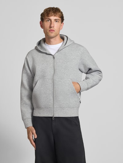 Männermodel trägt Relaxed Fit Sweatjacke mit Zweiwege-Reißverschluss von JACK & JONES, grau, elastisch, Känguru-Tasche, Ganzkörperansicht von vorne.