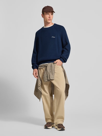 Mannelijk model draagt Relaxed Fit gebreide pullover uit puur katoen Model 'Campus' van PROHIBITED, ribboorden, ruglengte maat M 69 cm, mouwlengte maat M 98 cm, donkerblauw, zandkleurige broek, casual stijlen, volledig lichaamsaanzicht van voren.