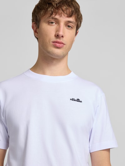 Męski model nosi T-Shirt mit Label-Stitching Modell 'ACCIANO CLASSIC' od Ellesse, biała bawełna, prosty krój, prążkowana stójka, wyhaftowane logo, długość tyłu w rozmiarze M: 67 cm, zbliżenie na górną część tułowia.