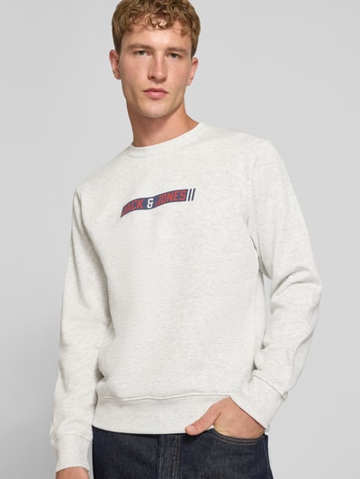 Männermodel trägt Regular Fit Sweatshirt mit Baumwoll-Anteil Modell 'Munk' von JACK & JONES, hellgrau, Logo-Print, Nahaufnahme Oberkörper. Rückenlänge 60 cm, Ärmellänge 67 cm, elastische Abschlüsse, Rundhalsausschnitt, Material-Mix.
