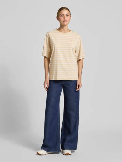 Frauenmodel trägt Oversized T-Shirt aus reiner Baumwolle Modell 'C_EREGULAR_STRIPE' von BOSS Orange mit Allover-Streifenmuster in Beige auf Jersey, Label Stitching, Ganzkörperansicht von vorne.