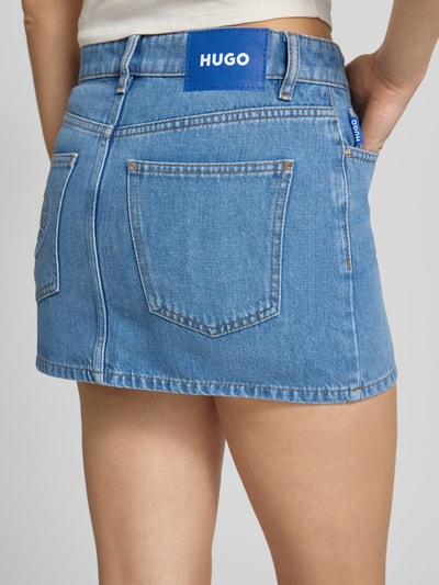 Frauenmodel trägt Regular Fit Jeansrock aus Baumwoll-Mix Modell 'GALANIE_B' von Hugo Blue in Denim-Optik mit Label-Patch, 5-Pocket-Design, Mini-Länge, verdecktem Reißverschluss, Gürtelschlaufen, gerade Saum, Nahaufnahme Rückansicht.