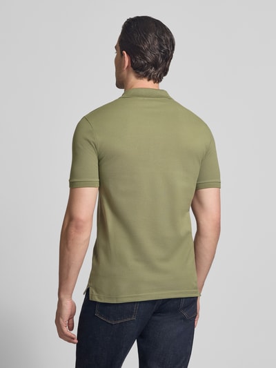 Męski model nosi Slim Fit Poloshirt aus reiner Baumwolle von Lacoste, jednokolorowy, krój slim fit, wyhaftowane logo, kołnierzyk polo, krótki rękaw, prążkowane zakończenie rękawów, zakończenie z rozcięciami po bokach, pika, bawełna, całkowity widok od tyłu.