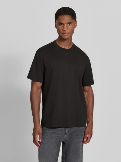 Männermodel trägt Regular Fit T-Shirt aus reiner Baumwolle von Lacoste in Schwarz, kombiniert mit grauer Jeans, Ganzkörperansicht von vorne. Herren T-Shirt von Lacoste