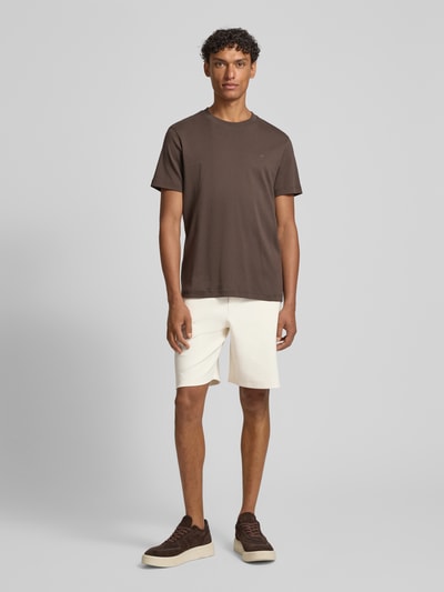 Męski model nosi szorty z wpuszczanymi kieszeniami model 'Joseignacio' od JOOP! Collection, mieszanka bawełny z dodatkiem streczu, krój loose fit, elastyczny pas z trokiem, naszywka z logo, szerokość w rozmiarze M 42 cm, długość wewnętrzna nogawki 22 cm, jasny kolor, gładka faktura, całkowity widok z przodu.