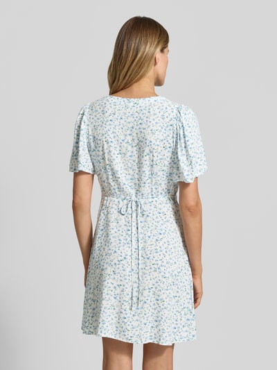 Frauenmodel trägt Leicht ausgestelltes Minikleid aus reiner Viskose Modell 'ALBA' von Vero Moda, Optik: Unifarben, Passform: Leicht, Mini-Länge, Ausschnitt: V-Ausschnitt, Taillengürtel, Verschluss: Knopfleiste, Ärmelform: Kurzarm, Material: Reine Viskose, zarte Blautöne mit kleinen Blumen, glatte Textur, Ganzkörperansicht Rückansicht.