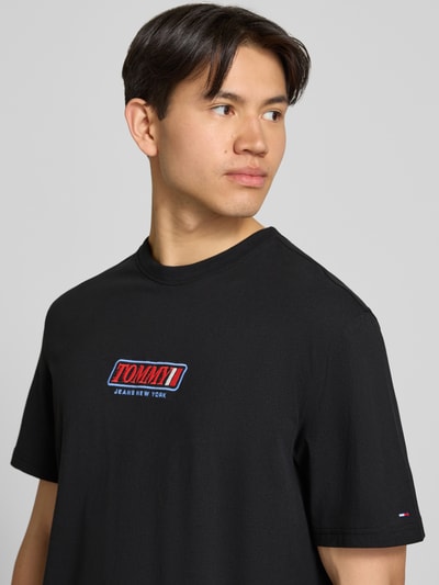 Männermodel trägt Regular Fit T-Shirt aus reiner Baumwolle von Tommy Jeans in Schwarz mit Label-Schriftzug, Nahaufnahme Oberkörper.