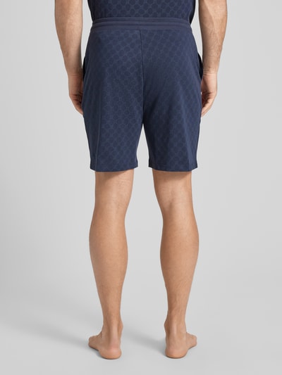 Männermodel trägt Shorts aus Baumwolle mit Logo-Muster von JOOP! Collection, dunkelblau, Regular-Fit, elastischer Bund, Ganzkörperansicht Rückansicht.