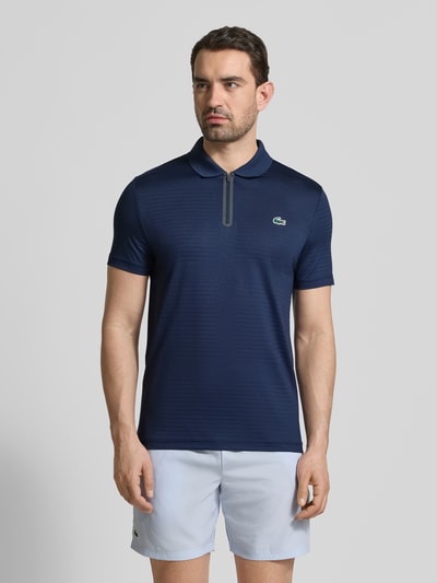 Männermodel trägt Slim Fit Poloshirt aus schnelltrocknendem Material von Lacoste, Optik: Unifarben, Logo-Patch, Polokragen, kurzer Reißverschluss, Ärmelform: Kurzarm, Ganzkörperansicht von vorne.
