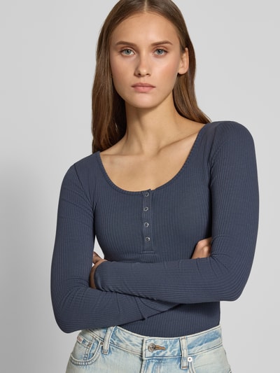 Frauenmodel trägt unifarbenes, dunkelblaues Slim Fit Langarmshirt aus Baumwoll-Mix Modell 'KITTE' von PIECES mit Henley-Ausschnitt und Rippenstruktur, Nahaufnahme Oberkörper.