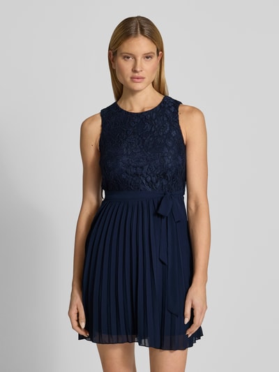 Modelka nosi Knielanges Kleid mit Spitze od Apricot, mieszanka materiałów z dodatkiem wiskozy, taliowany krój, długość do kolan, koronka, okrągły dekolt, wiązany pasek, spódnica z plisami, z tyłu wycięcie w kształcie łezki, długość tyłu w rozmiarze S: 91 cm, szerokość w rozmiarze S: 39 cm, ciemnoniebieski, gładka tekstura góry z koronką, matowy dół, widok na cały przód tułowia, zbliżenie na górę.