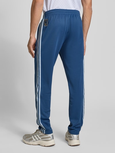 Mannelijk model draagt Regular Fit Sweatpants met katoenmodel 'FIGC OG' van adidas Originals, effen kleuren met contraststrepen, boord, materiaalmix met katoen, applicatie met labelstitching, sweatmateriaal, tunnelkoordsluiting, ganzekijk van achteren.