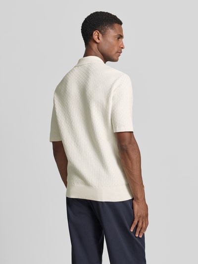 Męski model nosi koszulkę polo Regular Fit Poloshirt mit Strukturmuster Modell 'ARAAWEN' od Tiger Of Sweden z bawełny, krótki rękaw, kremowy kolor, kołnierzyk polo, fakturowany wzór, listwa guzikowa, długość tyłu w rozmiarze M: 68 cm, długość rękawów: 28 cm, widok całej sylwetki z tyłu.