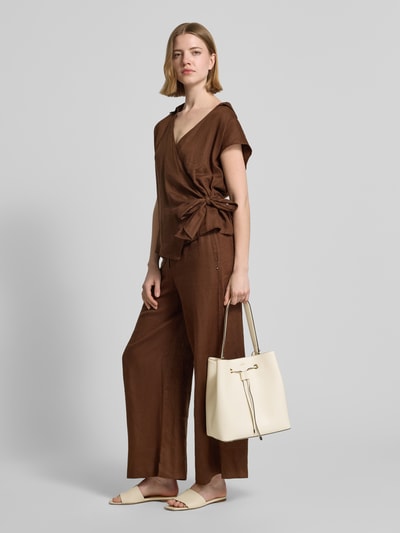 Modelka nosi Umhängetasche mit Label-Applikation Modell 'SANDY BUCKET' od BOSS w skórzanym wyglądzie, wykonana z imitacji skóry, kolor jasny, z rączką i zamkiem błyskawicznym, całkowity widok z przodu.