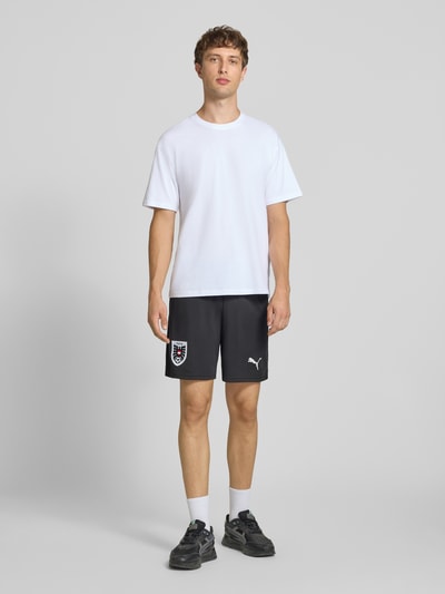 Männermodel trägt schwarze ÖFB Home Short Replica von PUMA PERFORMANCE mit elastischem Bund und Logo-Print, Ganzkörperansicht von vorne.