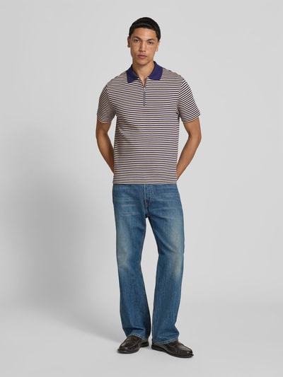 Männermodel trägt Slim Fit Poloshirt in Strick-Optik von Closed, Reine Baumwolle, Polokragen mit Reißverschluss, kurzärmelig, Rückenlänge 69 cm bei Größe M, Streifenmuster in Beige und Dunkelblau, Ganzkörperansicht von vorne.