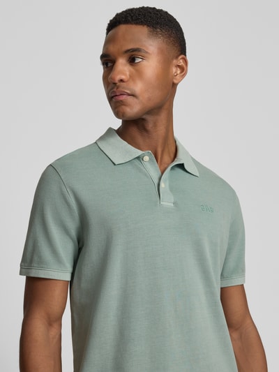Männermodel trägt Slim Fit Poloshirt mit Label-Stitching von GAP in Grün, Baumwoll-Elasthan-Mix, Nahaufnahme Oberkörper.