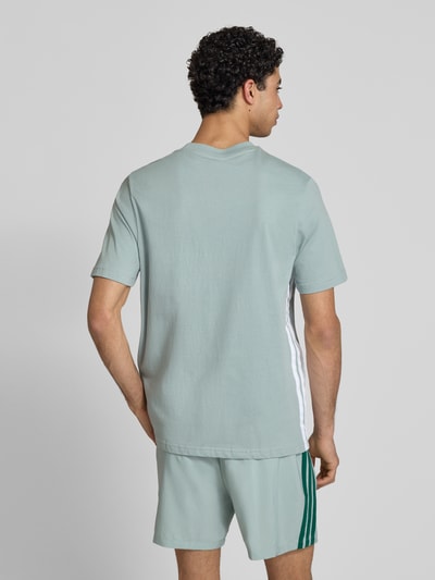 Männermodel trägt Regular Fit T-Shirt aus reiner Baumwolle von adidas Sportswear in Optik: Unifarben mit Logo-Stitching, Kontraststreifen, Ganzkörperansicht Rückansicht.