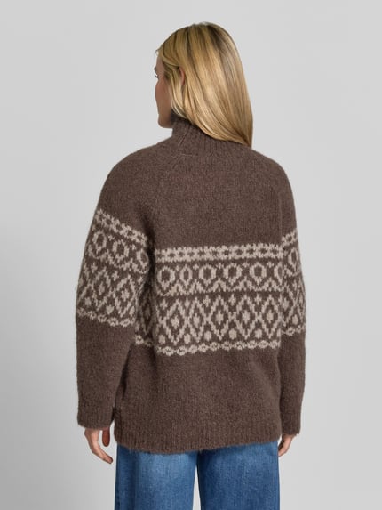 Frauenmodel trägt Pullover aus Alpaka mit Rollkragen Modell 'CRISTINE' von BAUM & PFERDGARTEN in brauner Strickoptik mit geometrischem Jacquardmuster, lange Raglanärmel und gerippte Abschlüsse, Ganzkörperansicht Rückansicht.