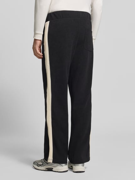 Männermodel trägt schwarze Straight Fit Sweatpants aus elastischem Material-Mix von RETERNITY mit cremefarbenen Seitenstreifen, Ganzkörperansicht Rückansicht.