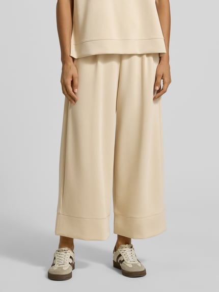 Frauenmodel trägt Wide Leg Sweatpants aus Modal-Mix von Rich & Royal in Beige, weite Form, elastischer Bund, Bundfalten, Seitentaschen, Nahaufnahme Oberschenkel bis Schuhe.