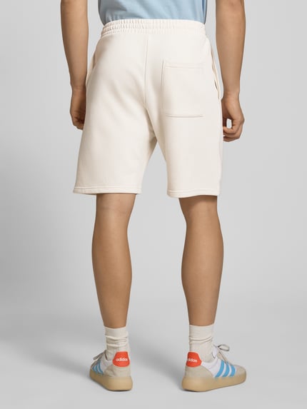 Männermodel trägt Regular Fit Shorts mit Label-Stitching von REVIEW aus Baumwoll-Mix, cremefarben, elastischer Bund, Ganzkörperansicht Rückansicht.