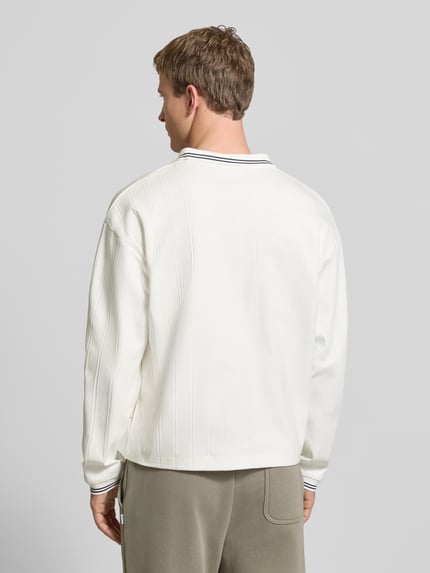 Männermodel trägt Strickpolo aus puur katoen Modell 'JORNIAGARA' von JACK & JONES in gebroken wit met labeldetail, losse pasvorm, ruglengte maat M 64 cm, Ganzkörperansicht Rückansicht.
