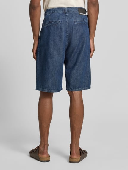 Männermodel trägt Regular Fit Jeans-Bermudas aus Baumwoll-Lyocell-Mix Modell 'DENIM' von Armedangels w stylizowanej na denim optyce, naszywka z logo, szlufki na pasek, zapięcie na guzik i ukryty zamek błyskawiczny, 5 kieszeni, mieszanka bawełny i lyocellu, Ganzkörperansicht Rückansicht.
