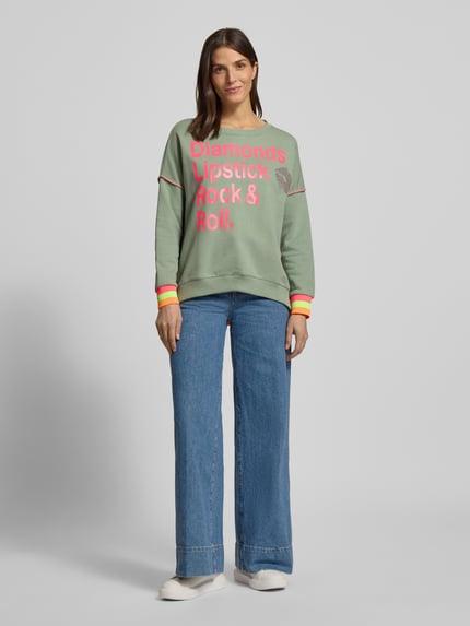 Frauenmodel trägt Oversized Sweatshirt mit gerippten Abschlüssen von miss goodlife in Grün mit pinkem Statement-Print, Ganzkörperansicht von vorne.