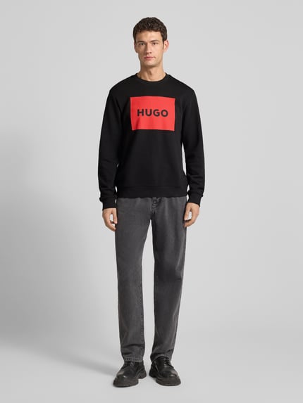 Männermodel trägt zwart Sweatshirt mit rode label-print, ronde hals, geribbelde boorden, losse pasvorm, pure katoen, Sweatshirt met Label-Print Modell 'Duragol' van HUGO, vooraanzicht volledige lichaamsfoto.