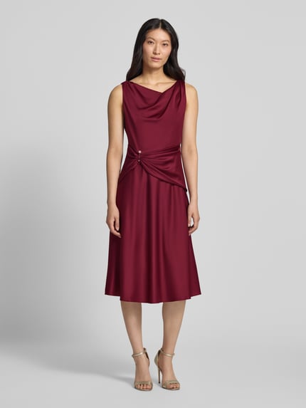 Frauenmodel trägt Cocktailkleid aus Satin mit Raffungen von Adrianna Papell in Bordeaux, taillierte Passform, Midilänge, Ganzkörperansicht von vorne.