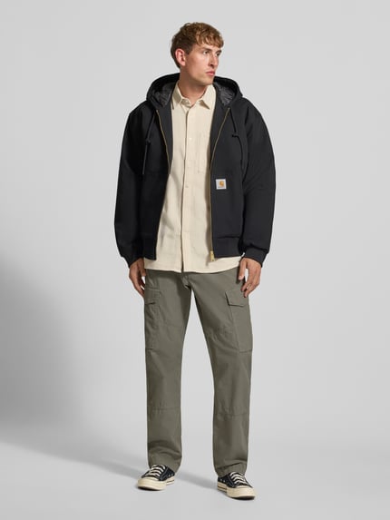 Männermodel trägt Regular Fit Cargohose aus reiner Baumwolle von G-Star RAW in hellem Khaki, kombiniert mit heller Jacke, Ganzkörperansicht von vorne.