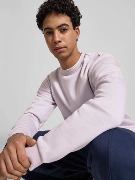Männermodel trägt Regular Fit Sweatshirt aus katoenmix model 'CERES' van Only & Sons, effen lichtroze, ronde hals, lange mouw, label patch, geribde boorden, sweatmateriaal; close-up bovenlichaam vooraanzicht.