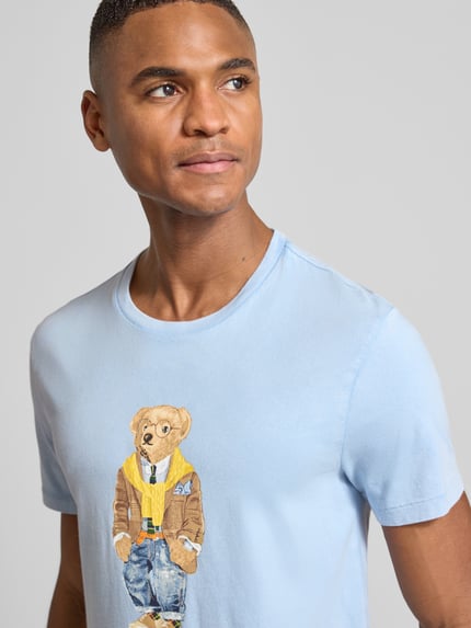 Mężczyznamodel nosi T-Shirt mit Label-Print von Polo Ralph Lauren ze 100% bawełny, slim fit, jasnoniebieski, nadruk z misiem, zbliżenie na górę ciała.