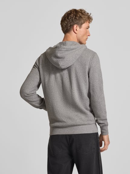 Männermodel trägt Regular Fit Sweatjacke aus Baumwoll-Mix mit Label-Detail von Superdry in Grau, Rückansicht, Ganzkörperansicht Rückansicht. Rückenlänge und Ärmellänge je 65 cm, Kapuze mit Tunnelzug, elastische Abschlüsse und geteilte Kängurutasche.