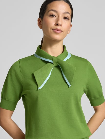 Frauenmodel trägt Regular Fit Poloshirt aus Viskose-Mix Modell 'JONDA' von Essentiel Antwerp, Optik: Unifarben, Kontraststreifen, Polokragen mit Schleife, Kurzarm, Ärmelabschluss und Rumpfabschluss gerippt, Materialverarbeitung: Taschen, Nahaufnahme Oberkörper.