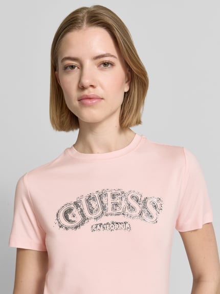Modelka kobieca nosi T-Shirt aus Viskose-Elasthan-Mix mit Logo von Guess Activewear, jasnoróżowy kolor, krój regular fit, okrągły dekolt, długość tyłu w rozmiarze S: 53 cm, z widocznym logo, tekstura gładka, zbliżenie na górną część ciała