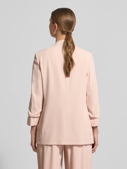 Modelka kobieca nosi żakiet 'Blazer mit Pattentaschen' od Jake*s Collection, mieszanka materiałów z dodatkiem streczu, luźny krój, stójka, kieszenie z patką, rękaw o dł. 3/4, długość tyłu w rozmiarze 36: 69 cm, szerokość w rozmiarze 36: 44 cm, długość rękawów w rozmiarze 36: 52 cm, jasnoróżowy, gładki, widok całej sylwetki od tyłu.