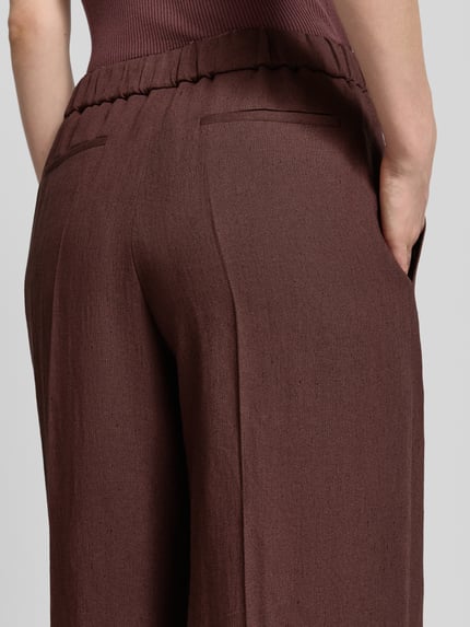 Kobieta nosi spodnie Relaxed Fit Hose aus Leinen-Mix model 'TIANA11' od BOSS, efekt: jednolity kolor, kanty, materiał: mieszanka lnu i wiskozy, lamowane kieszenie, ściągacz, zapięcie na haftkę i zamek błyskawiczny, widoczne wpuszczane kieszenie boczne, detal: tylne kieszenie z wypustkami, ujęcie: z tyłu, zbliżenie na biodra.