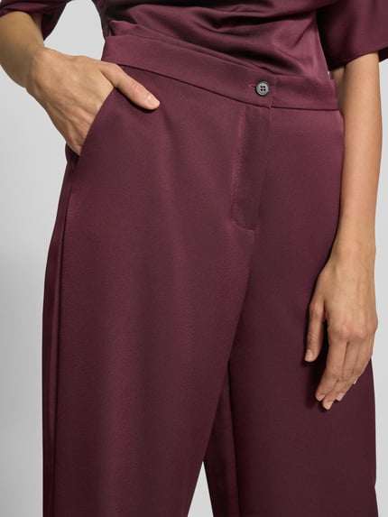 Frauenmodel trägt Stoffhose mit Knopf- und Reißverschluss von Swing in Bordeaux, lockerer Schnitt, französische Eingrifftaschen, Nahaufnahme Oberkörper.