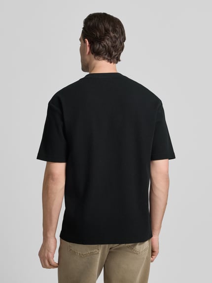 Männermodel trägt Regular Fit T-Shirt aus reiner Baumwolle Modell 'DAFFL' von HUGO in Schwarz, strukturierte Optik, Ganzkörperansicht Rückansicht.