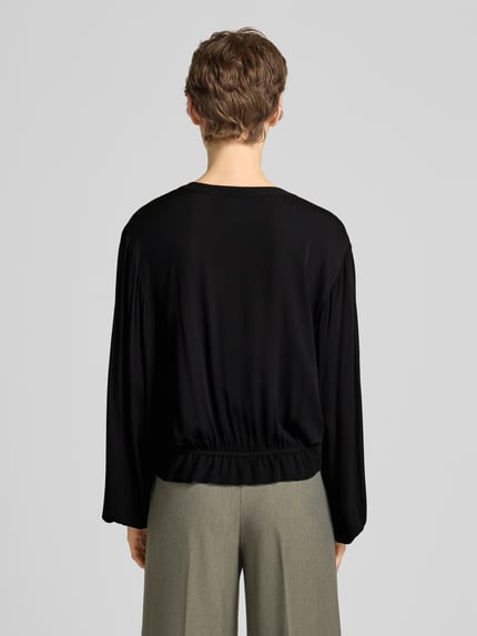Frauenmodel trägt Bluse aus Viskose mit Schlüsselloch-Ausschnitt von Emily Van den Bergh in Schwarz, elastische Abschlüsse, Ganzkörperansicht Rückansicht.