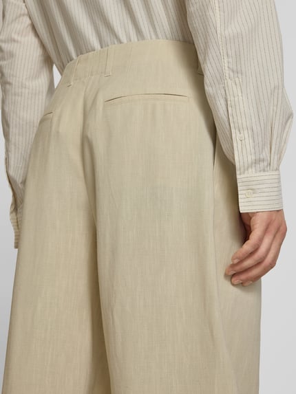Männermodel trägt Stoffhose aus Viskose-Leinen-Mix von MAISON KITSUNÉ in Beige mit Kellerfalten, Nahaufnahme Rückansicht