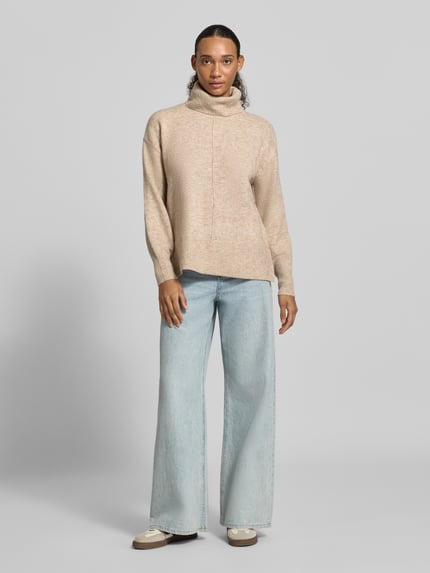 Frauenmodel trägt Rollkragenpullover mit gerippten Abschlüssen von PIECES in melange Beige, Feinstrick, kombiniert mit weiter Jeans, Ganzkörperansicht von vorne.