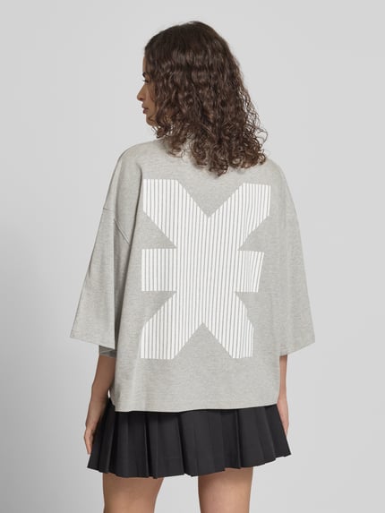 Vrouwenmodel draagt Oversized T-Shirt met Rundhalsausschnitt van Karo Kauer in lichtgrijs, labelprint, pure katoen, cropped fit, ruglengte 61 cm, achteraanzicht volledig.