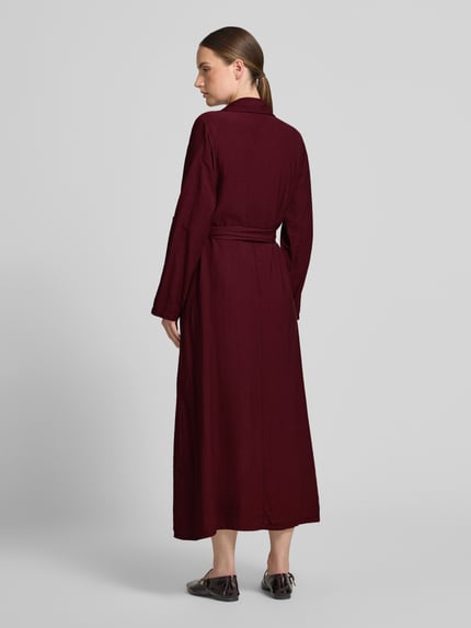 Frauenmodel trägt Hemdblusenkleid mit kurzer Knopfleiste Modell 'Di44anaa' von ZABAIONE, bordeaux, tailliert, Maxilänge, Rückenansicht.