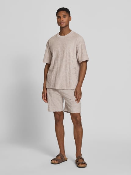 Männermodel trägt Regular Fit T-Shirt aus Baumwoll-Mix Modell 'TE_FLOWER' von BOSS Orange, beigefarben mit Allover-Strukturmuster, Ganzkörperansicht von vorne.